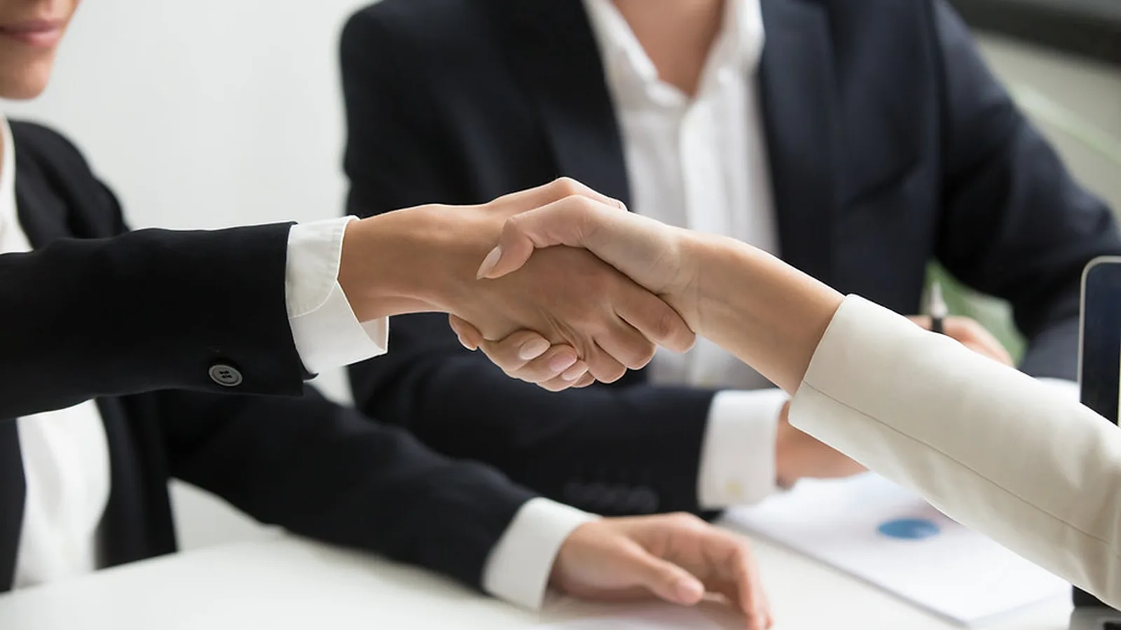 Two professionals shaking hands across a table at the close of a business meeting
